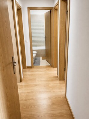 A hallway with wooden flooring leading to a bathroom with a toilet and a window with blinds. - Room-singh Leite Holiday Home Cosy Room (Lisbon)