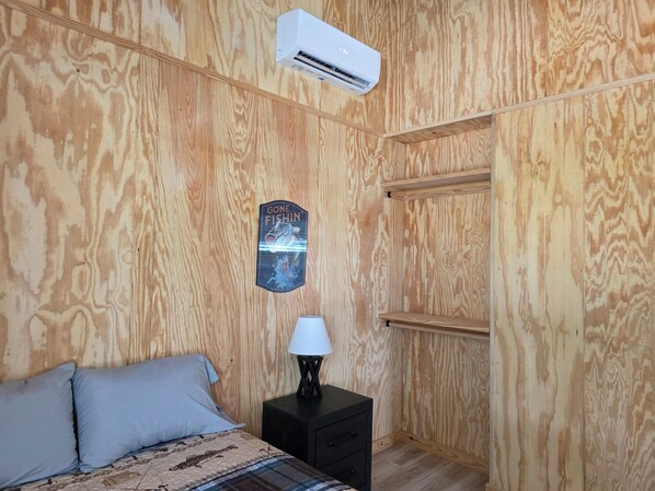 A room with a bed, a nightstand, a lamp, an air conditioner, and a wooden wall with a fish-themed decoration.