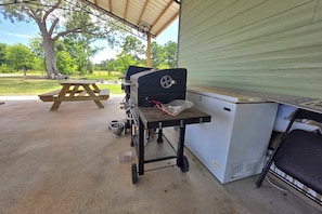 An outdoor patio with a barbecue grill, a picnic table, and a water dispenser.