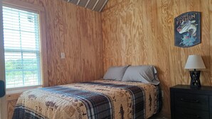 A bedroom with a wooden paneled wall, a bed with a patterned bedspread, a nightstand with a lamp, and a wall decoration. - The Crappie Cabin #5
When a tent just won't do! (Abbeville)