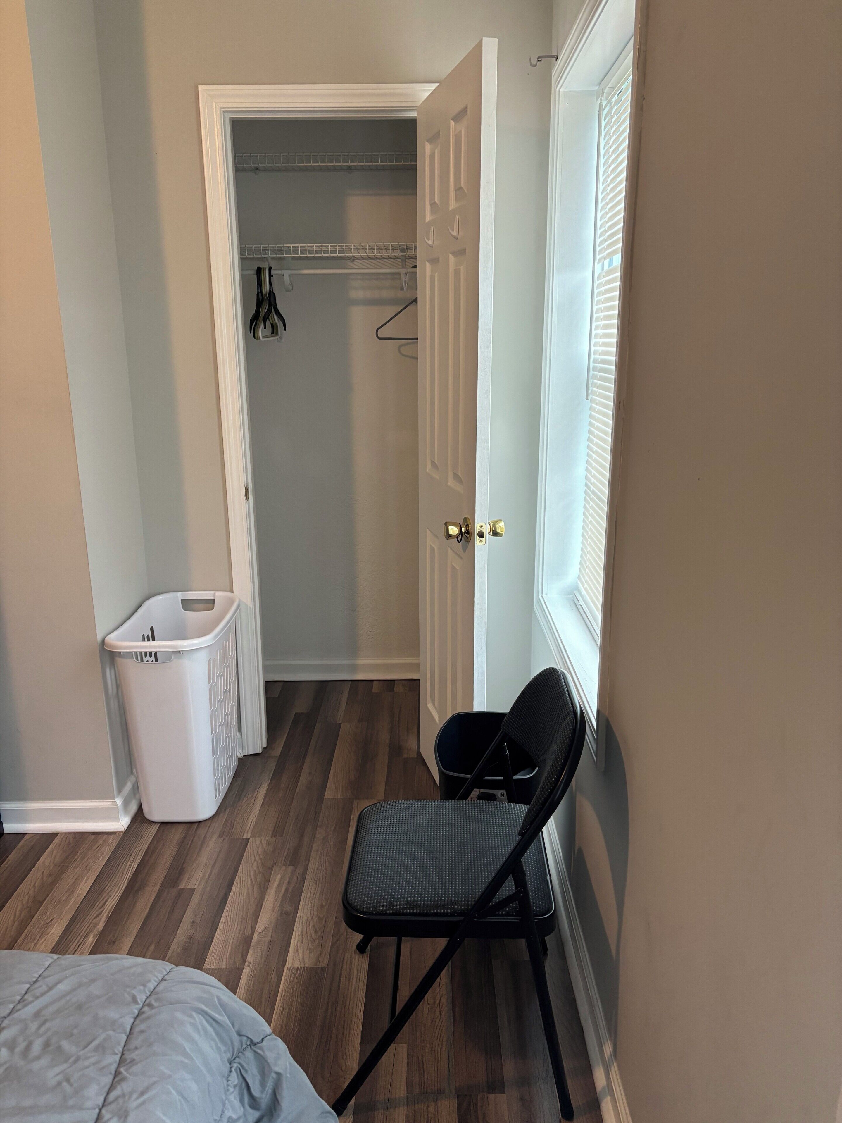 Un dormitorio con cama, una silla, un cesto de ropa y un armario con puerta.