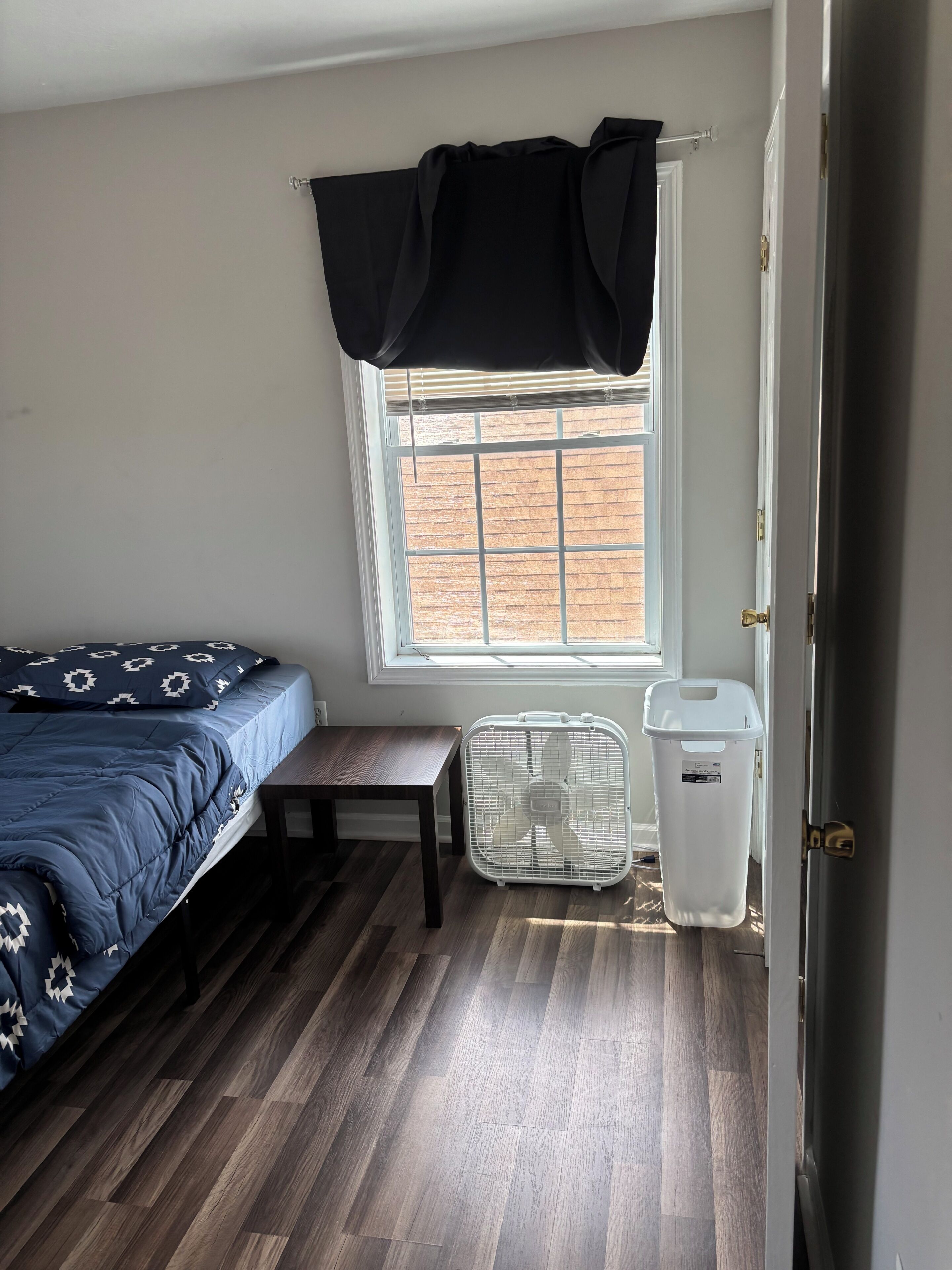 A bedroom with a bed, a window with a view, a bench, and a trash bin.