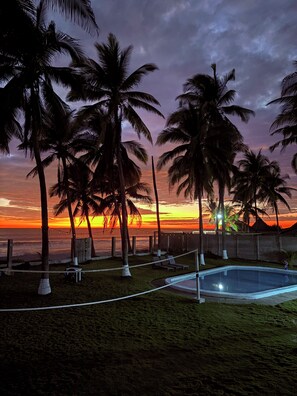 A pool area with lounge chairs and a volleyball net, surrounded by palm trees and a sunset view. - El Pimental House, CA (San Luis Talpa)