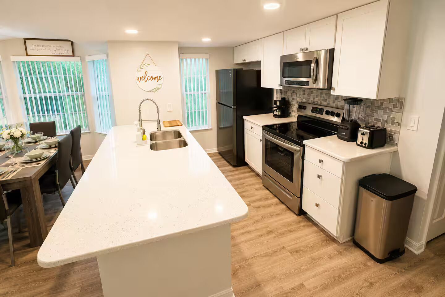 Cocina moderna con una isla central, electrodomésticos de acero inoxidable y encimera blanca.
