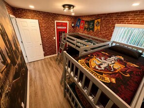 A room with a brick wall, a white door, a red telephone booth, and a bunk bed with a Gryffindor-themed bedspread. - Family Getaway Near Disney • Pool & Hot Tub (Kissimmee)