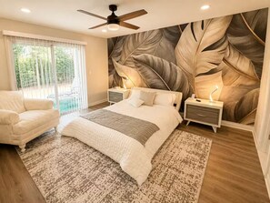 A bedroom with a large bed, a ceiling fan, a nightstand, and a view of a pool through the window. - Family Getaway Near Disney • Pool & Hot Tub (Kissimmee)
