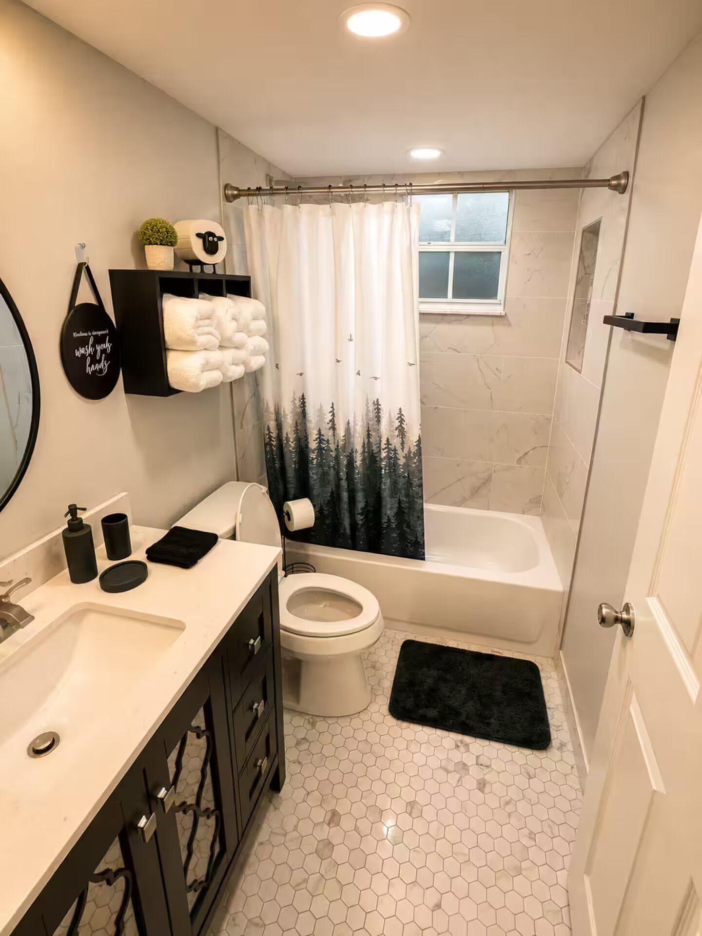 A bathroom with a toilet, a bathtub, a sink, and a mirror. There is a towel rack with towels and a shower curtain with a forest print.