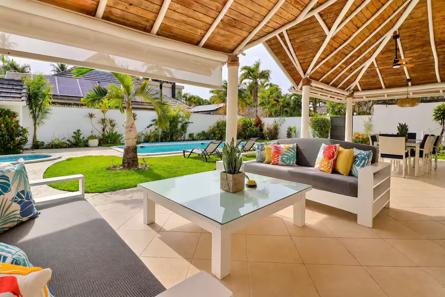 Un patio exterior con piscina, mobiliario, y una zona cubierta con mesa y sofá.