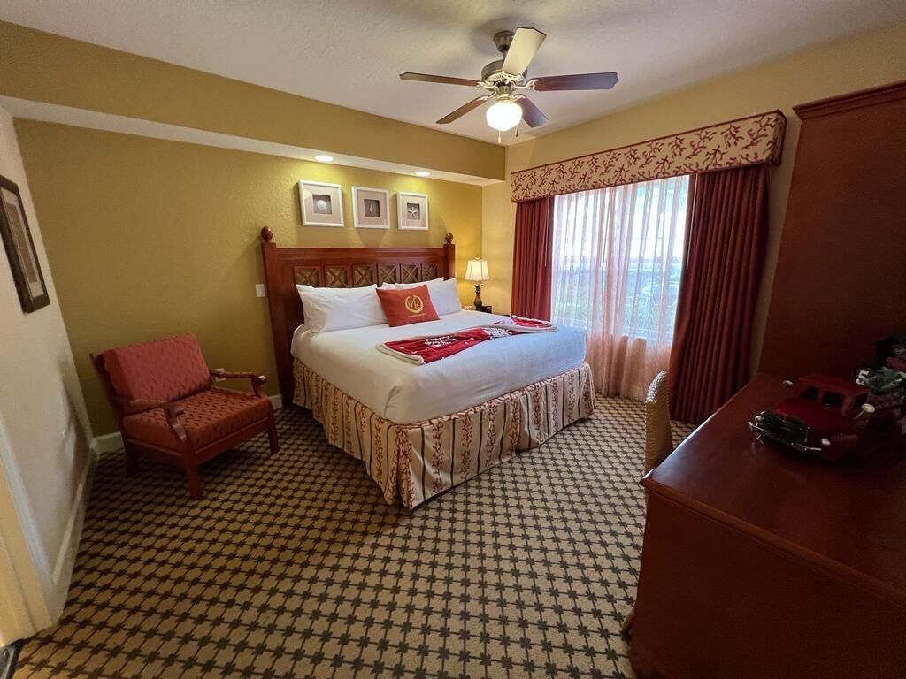 A hotel room with a bed, a chair, a desk, and a ceiling fan.
