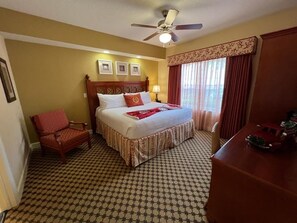 Quarto de hotel com uma cama, uma cadeira, uma mesa e um ventilador de teto.