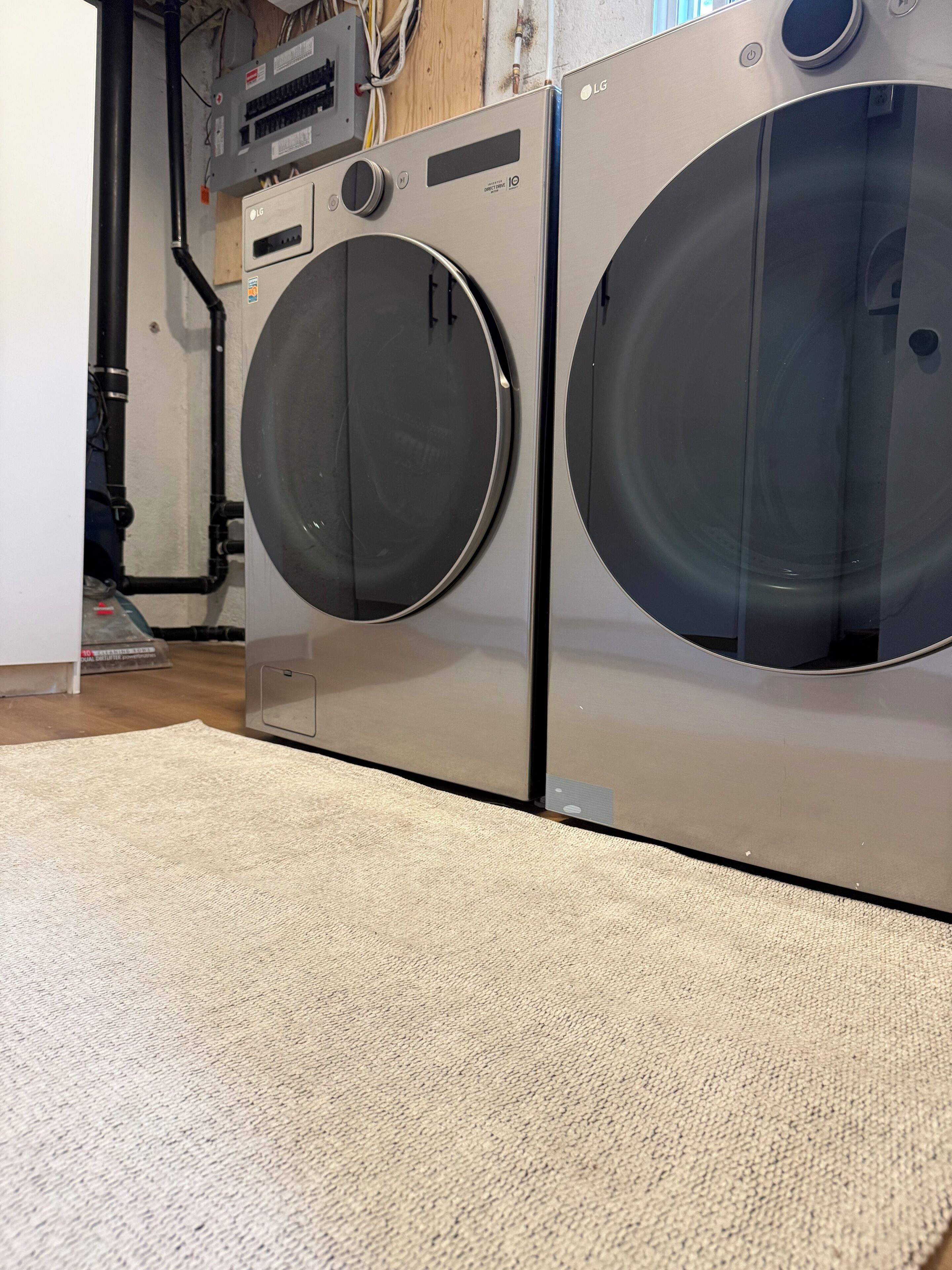 Two front-loading washing machines with a beige carpet in front.