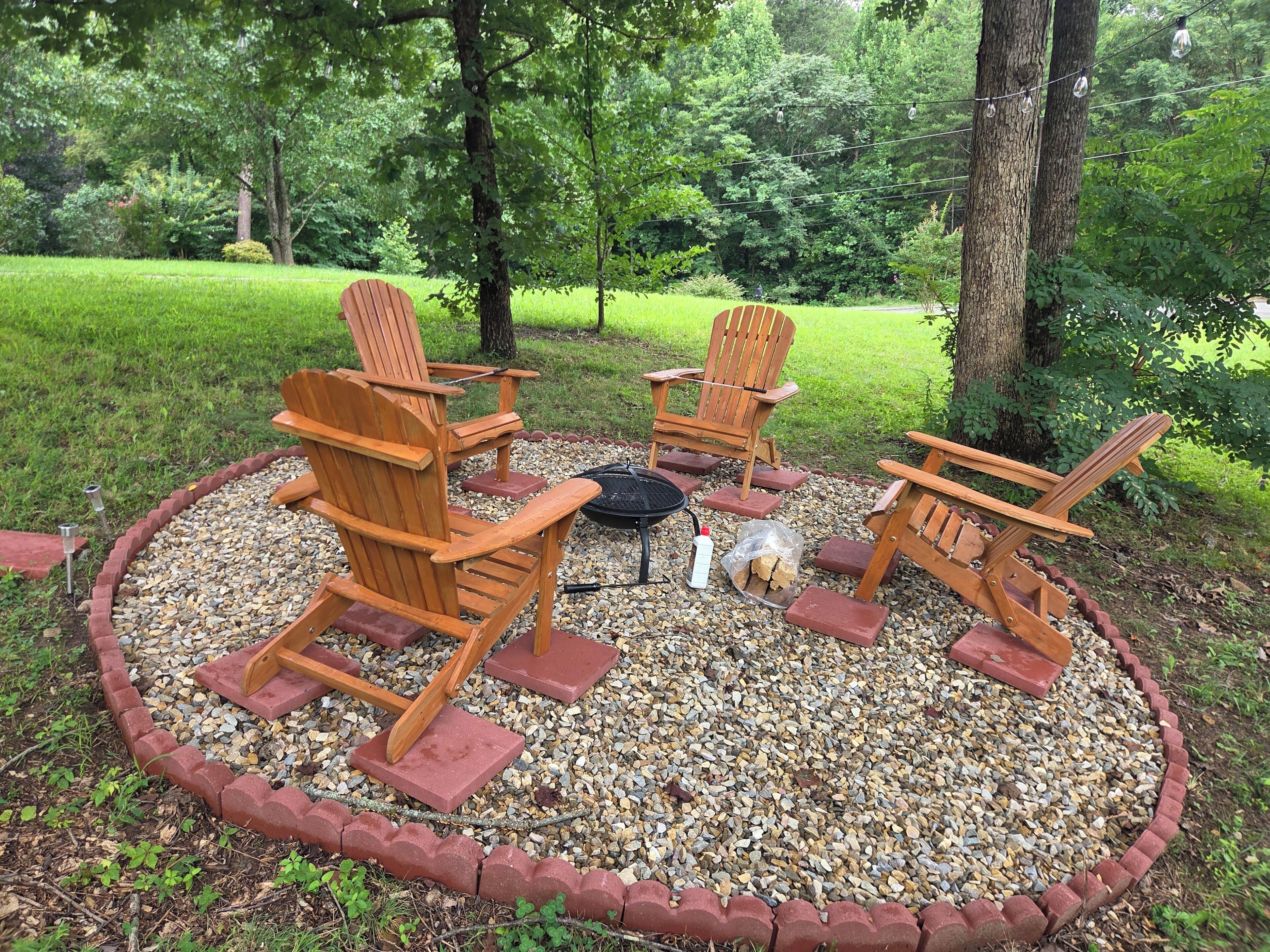 A circular outdoor seating area with four wooden Adirondack chairs, a fire pit, and a gravel border.