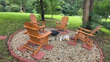 A circular outdoor seating area with four wooden Adirondack chairs, a fire pit, and a gravel border.