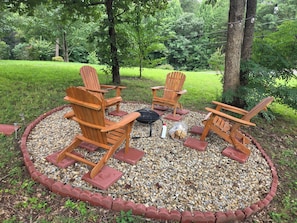 A circular outdoor seating area with four wooden Adirondack chairs, a fire pit, and a gravel border. - Cozy Mountain Retreat - Private Hot Tub & Fire Pit (Sevierville)
