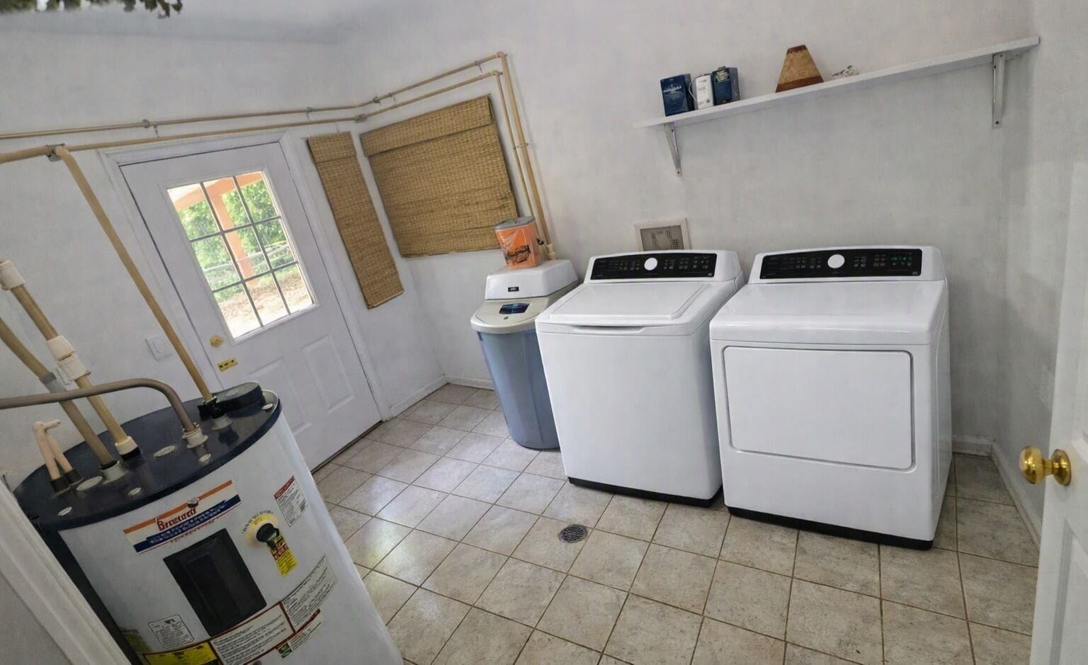 A laundry room with two white washing machines, a water heater, and a trash can.