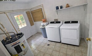 A laundry room with two white washing machines, a water heater, and a trash can. - Cozy Mountain Retreat - Private Hot Tub & Fire Pit (Sevierville)