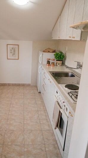 A compact kitchen with white cabinets, a gas stove, a sink, and a small countertop area. - Apartment Duka "for 5" - 100m sandy beach + panoramic sea view + AirCon. & WiFi. (Lumbarda)