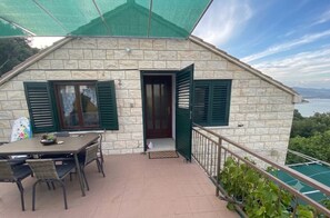 A stone building with a balcony, a table with chairs, and a view of the sea. - Apartment Duka "for 5" - 100m sandy beach + panoramic sea view + AirCon. & WiFi. (Lumbarda)