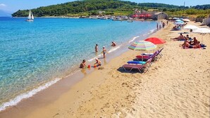 Ein Strand mit klarem Wasser, einer Segelyacht und Menschen, die das Ufer genießen.
