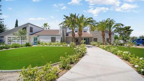 Una propiedad residencial con entrada pavimentada, césped cuidado y palmeras.