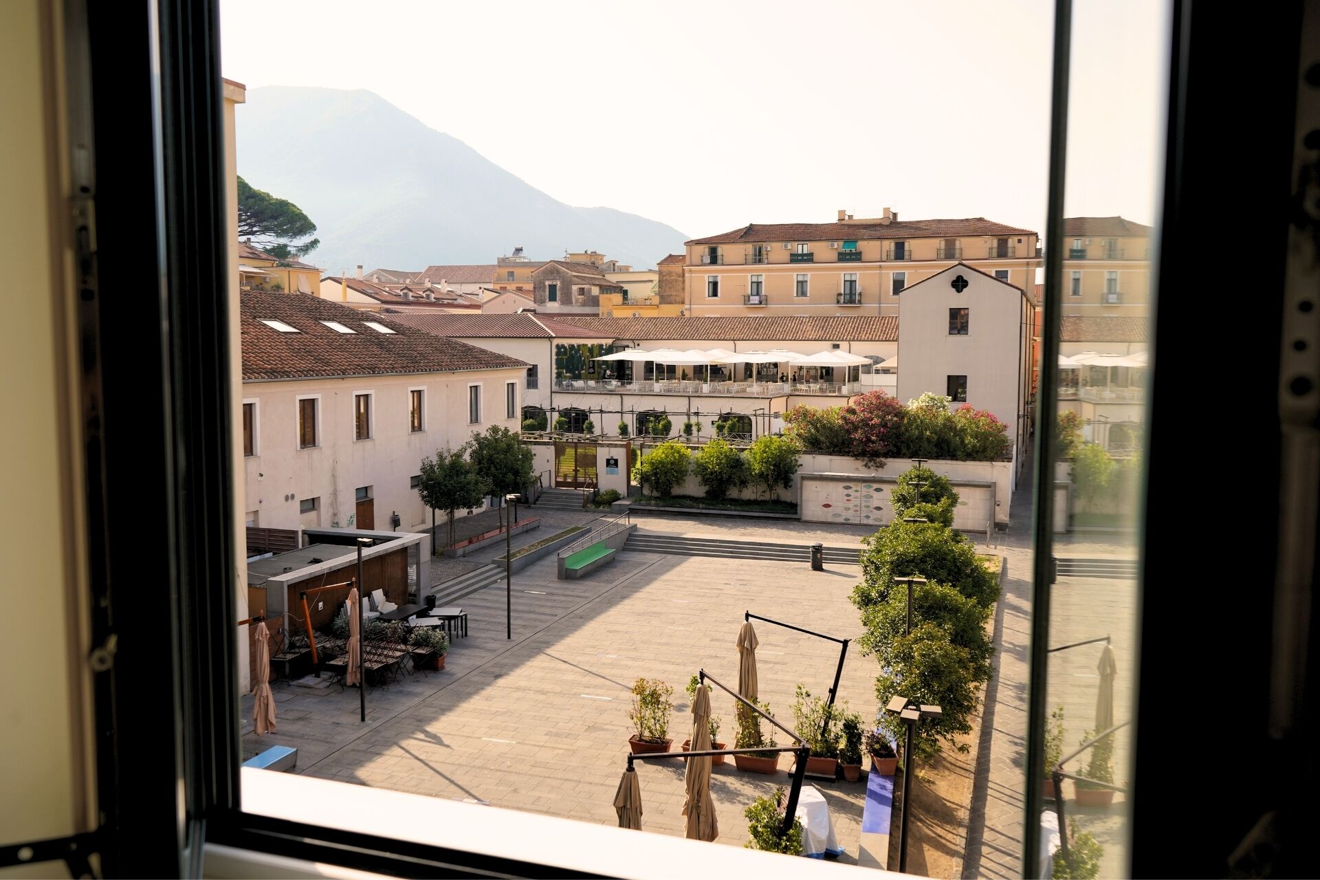 A courtyard with outdoor seating, a building with a terrace, and a mountain in the background.