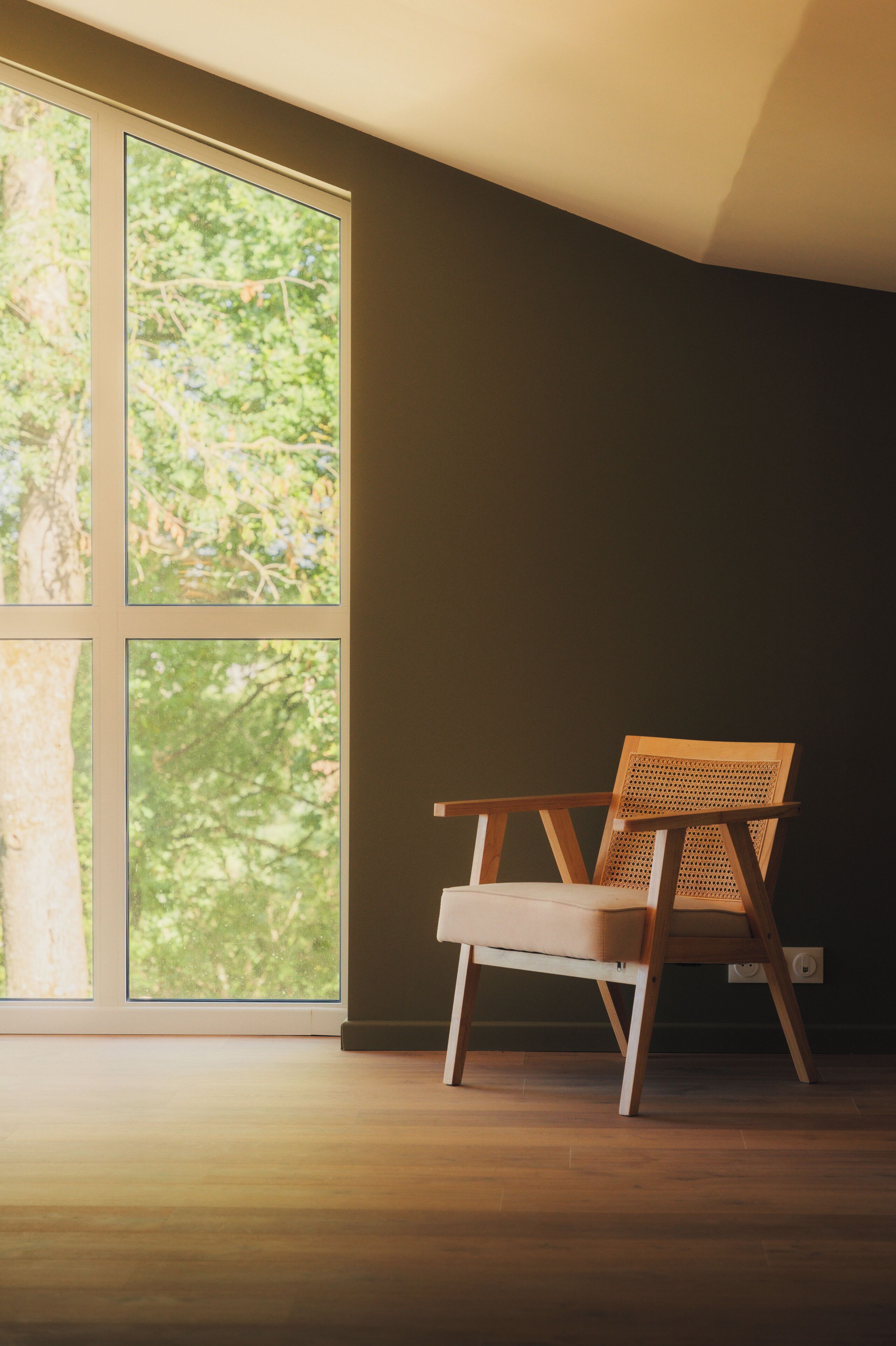 A room with a large window, a wooden chair, and a dark wall.