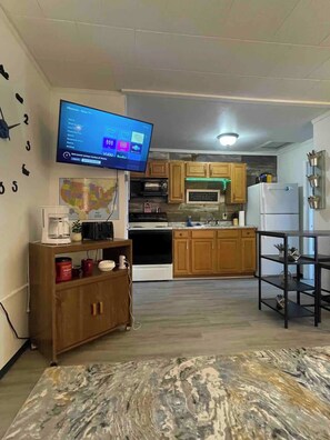 A modern kitchen with wooden cabinets, a microwave, and a refrigerator. A flat-screen TV is mounted on the wall displaying a home screen.
