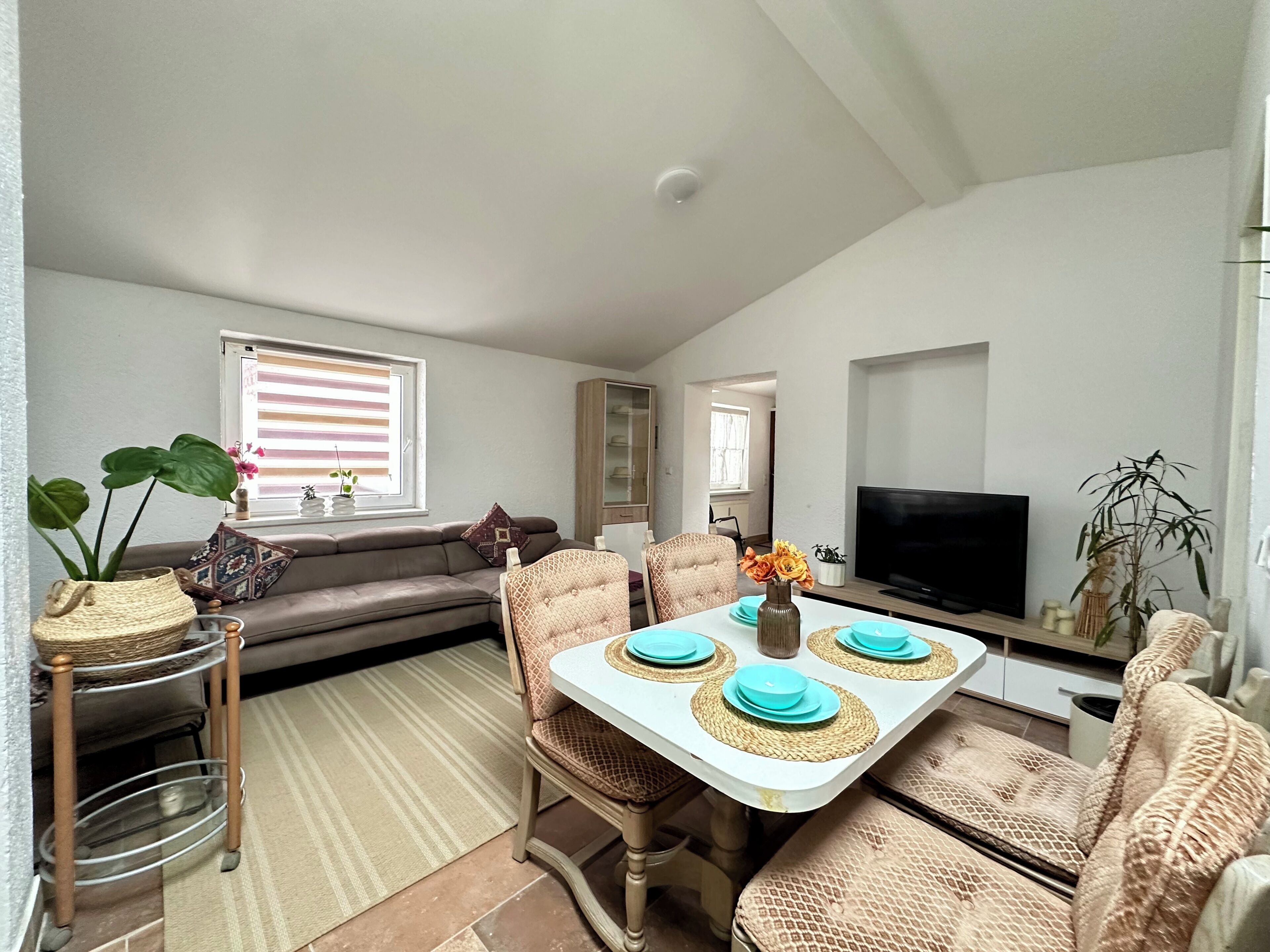 A dining area with a table set for four, a sofa, and a television.
