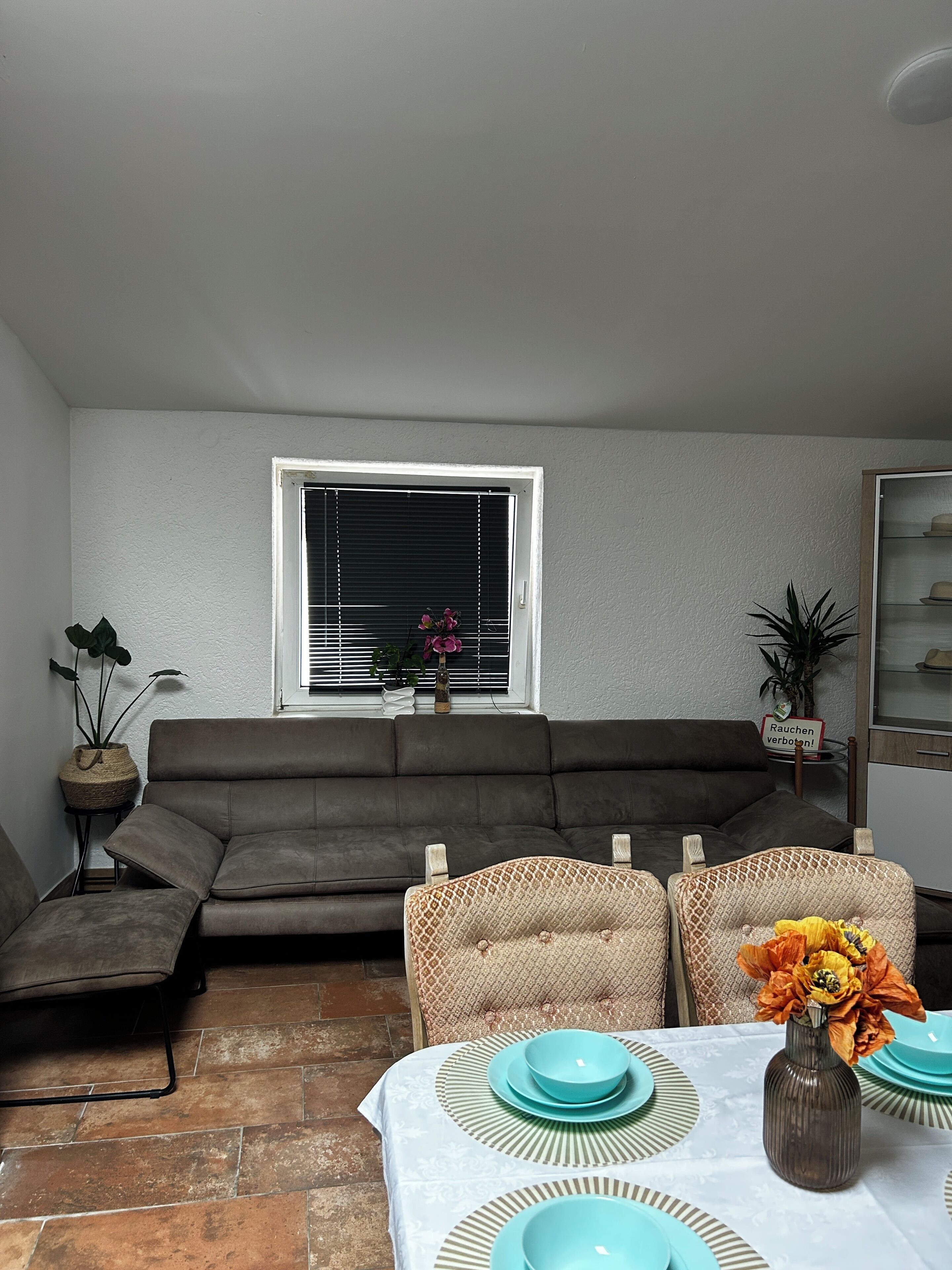 A living room with a sofa, a dining table set with plates, and a window with blinds.