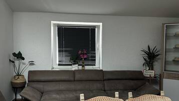 A living room with a sofa, a dining table set with plates, and a window with blinds.
