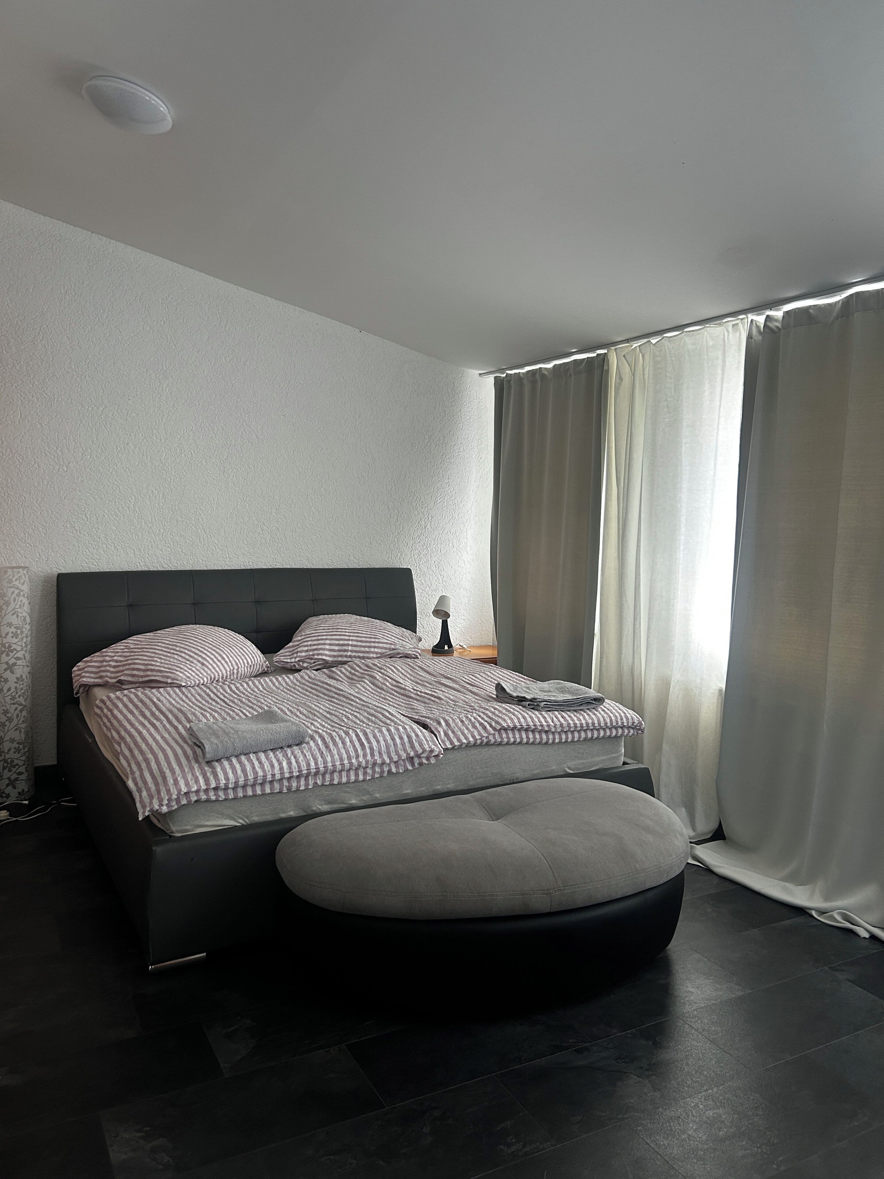 Un dormitorio moderno con una cama grande, una mesita de noche con lámpara y una ventana con cortinas.