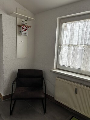 A room with a radiator, a window with lace curtains, a chair, and a sign prohibiting smoking. - Modern apartment that sleeps 6 (Weißenfels)