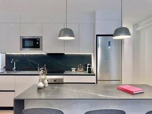 A modern kitchen with a marble countertop, a built-in microwave, a stainless steel refrigerator, and pendant lighting. - 3-Bedroom Apartment in Salamanca with a Private Terrace (Madrid)
