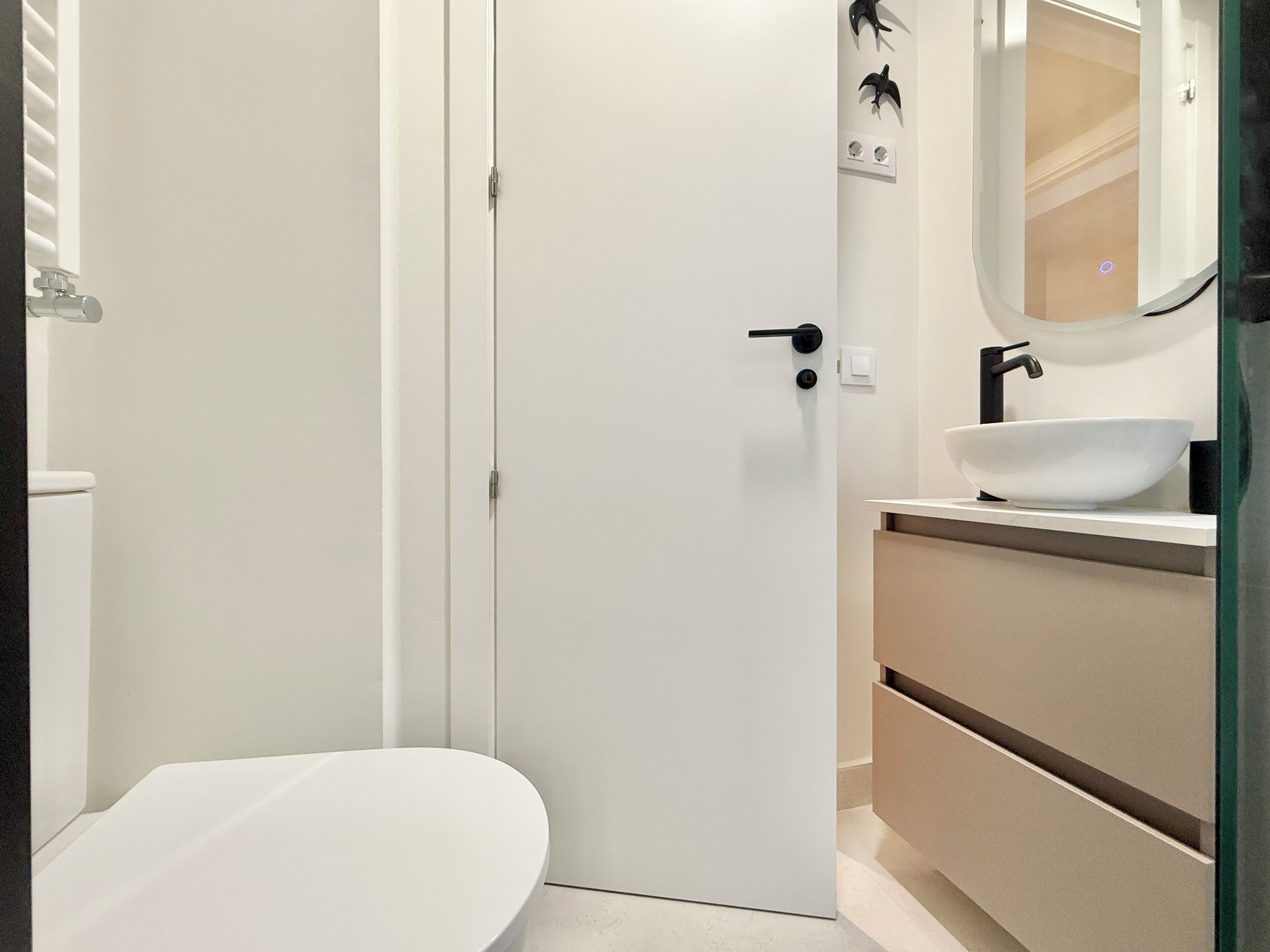 Ein modernes Badezimmer mit einer weißen Toilette, einem weißen Waschbecken mit einem schwarzen Wasserhahn und einem Spiegel darüber.
