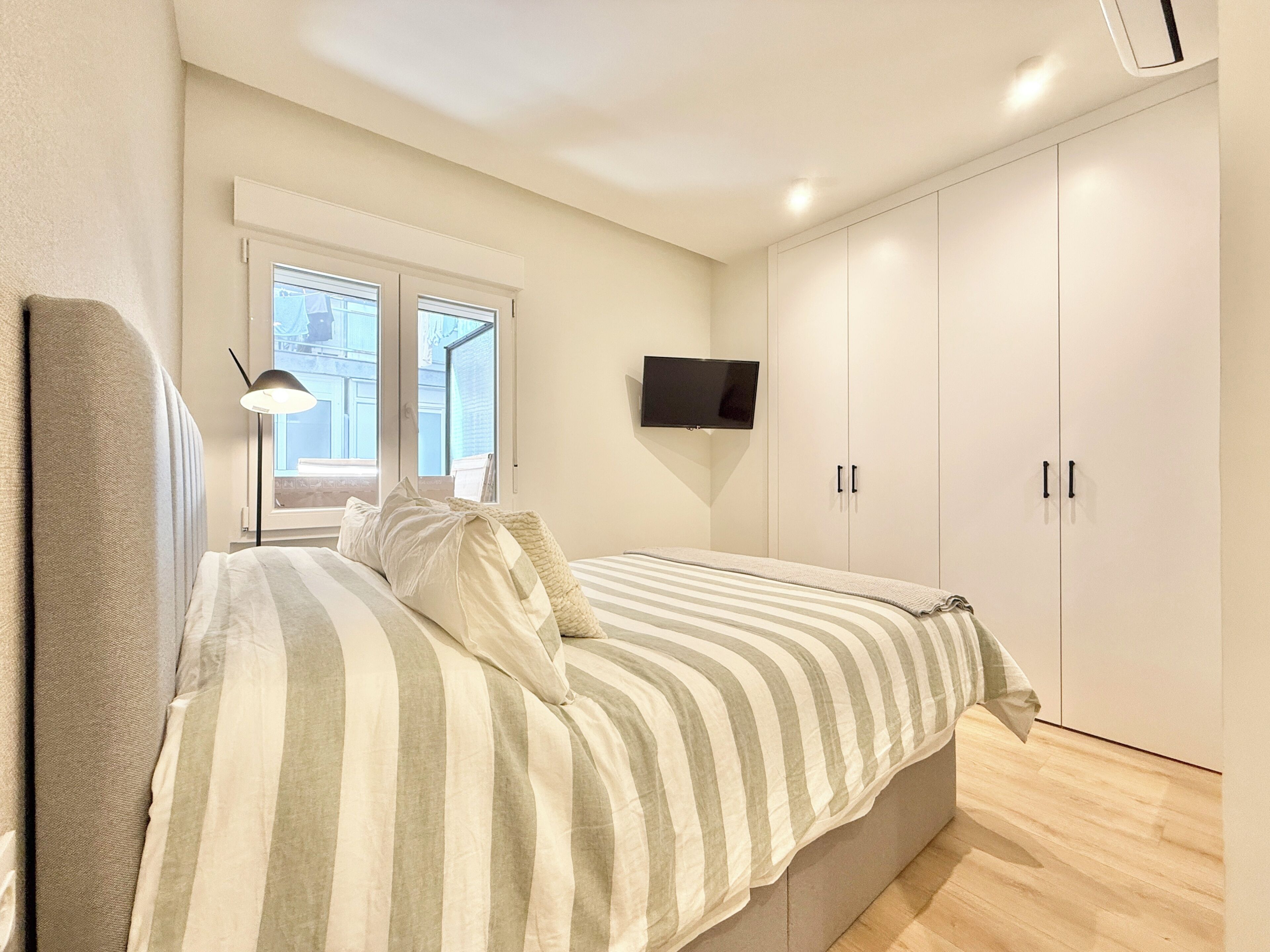 A bedroom with a bed, a TV mounted on the wall, and a wardrobe.
