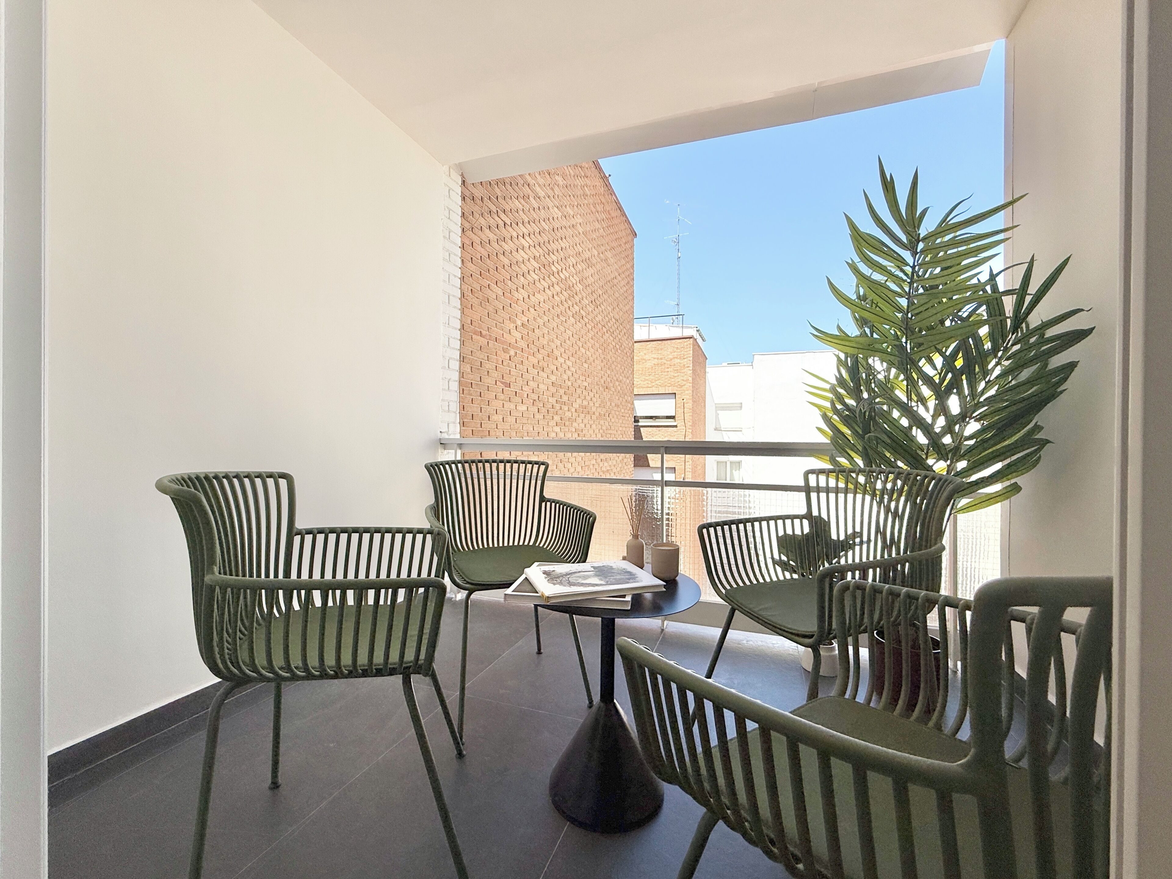 Un balcón con una mesa, sillas, una planta en maceta y vistas a edificios.