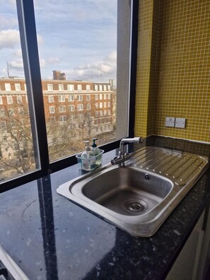 Eine Küche mit einem Edelstahlspülbecken, einem Fenster mit Blick auf Gebäude und einer gelben, gefliesten Rückwand.
