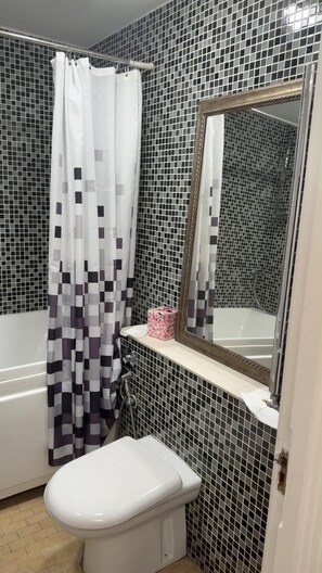 A bathroom with a white toilet, a shower with a black and white checkered curtain, and a mirror above the sink. - Charming Dartford Apartment With a View (Dartford)