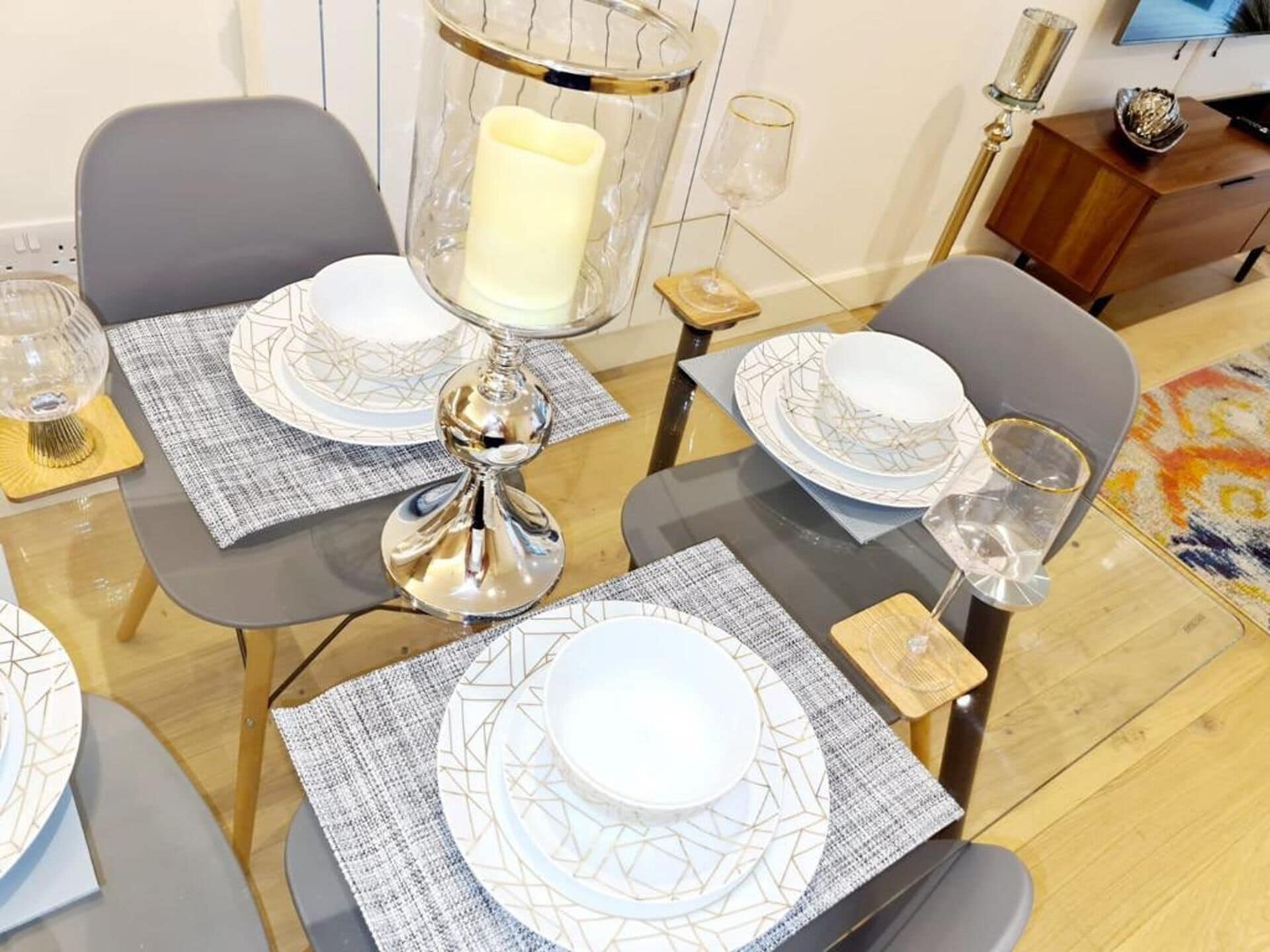 A dining table set with white plates, geometric-patterned placemats, and a candle in a glass holder.