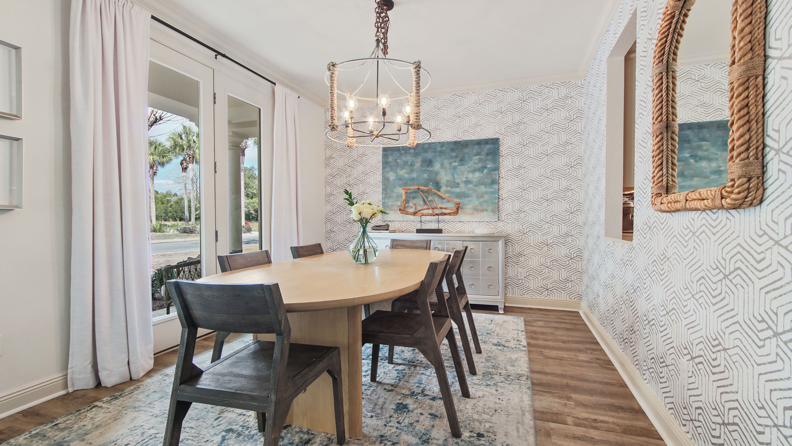 Une salle à manger avec une table ronde, des chaises, un lustre et une vue sur l’extérieur à travers les portes vitrées.