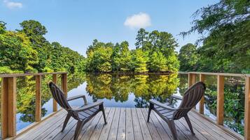 A wooden deck with two chairs facing a calm lake surrounded by dense greenery.
