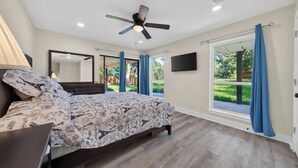 A bedroom with a bed, a ceiling fan, a TV, and a view of the outdoors.