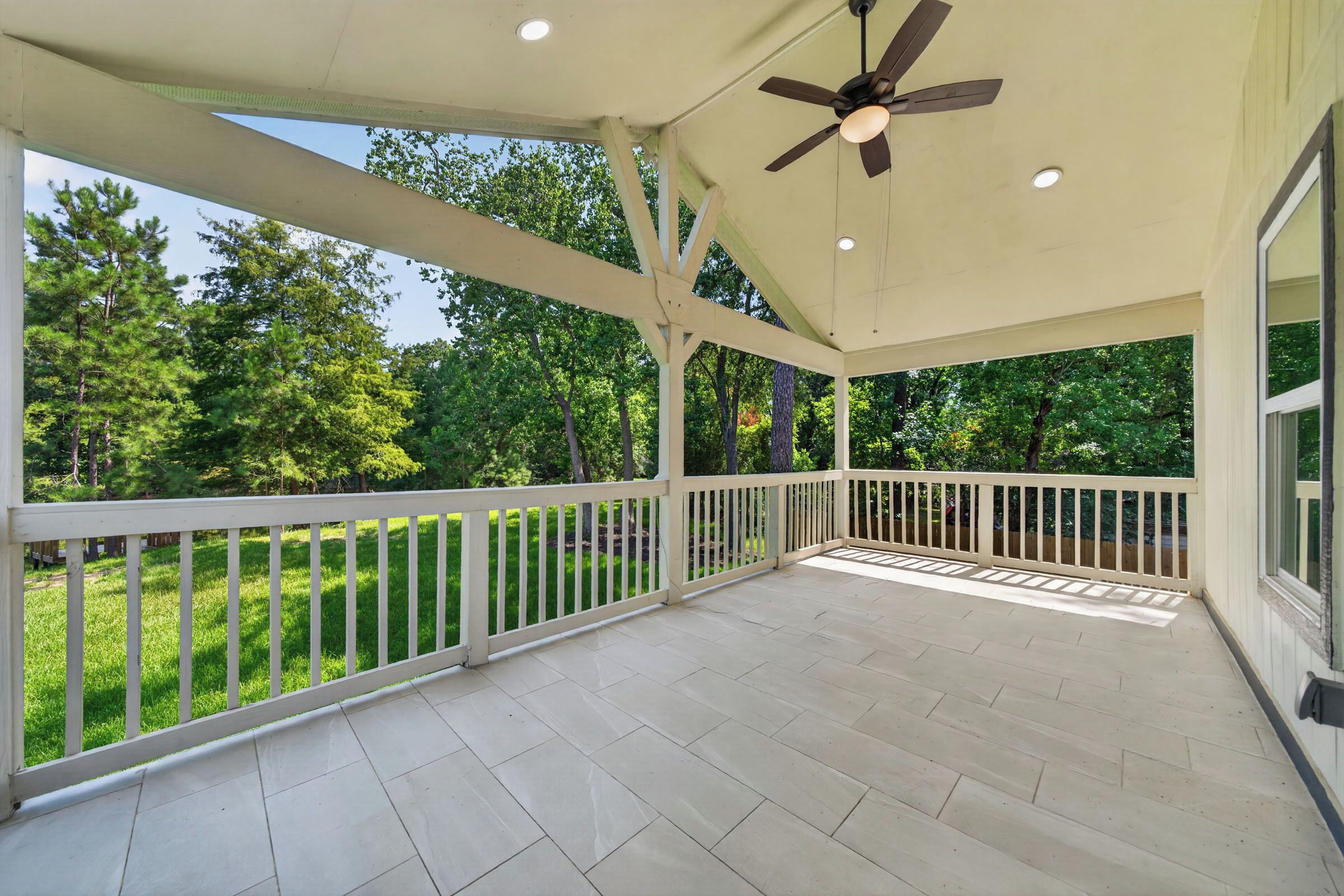 A covered outdoor area with a ceiling fan, white railings, and a view of a green landscape.