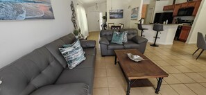 A living room with a sofa and two armchairs, a wooden coffee table, and a dining area with a table and chairs. - Luxury Disney Vacation Home Private Pool Resort Amenities Sleeps 8 Game Room (Kissimmee)