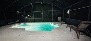 A swimming pool with a curved edge, surrounded by lounge chairs and a covered area with a glass ceiling. - Luxury Disney Vacation Home Private Pool Resort Amenities Sleeps 8 Game Room (Kissimmee)