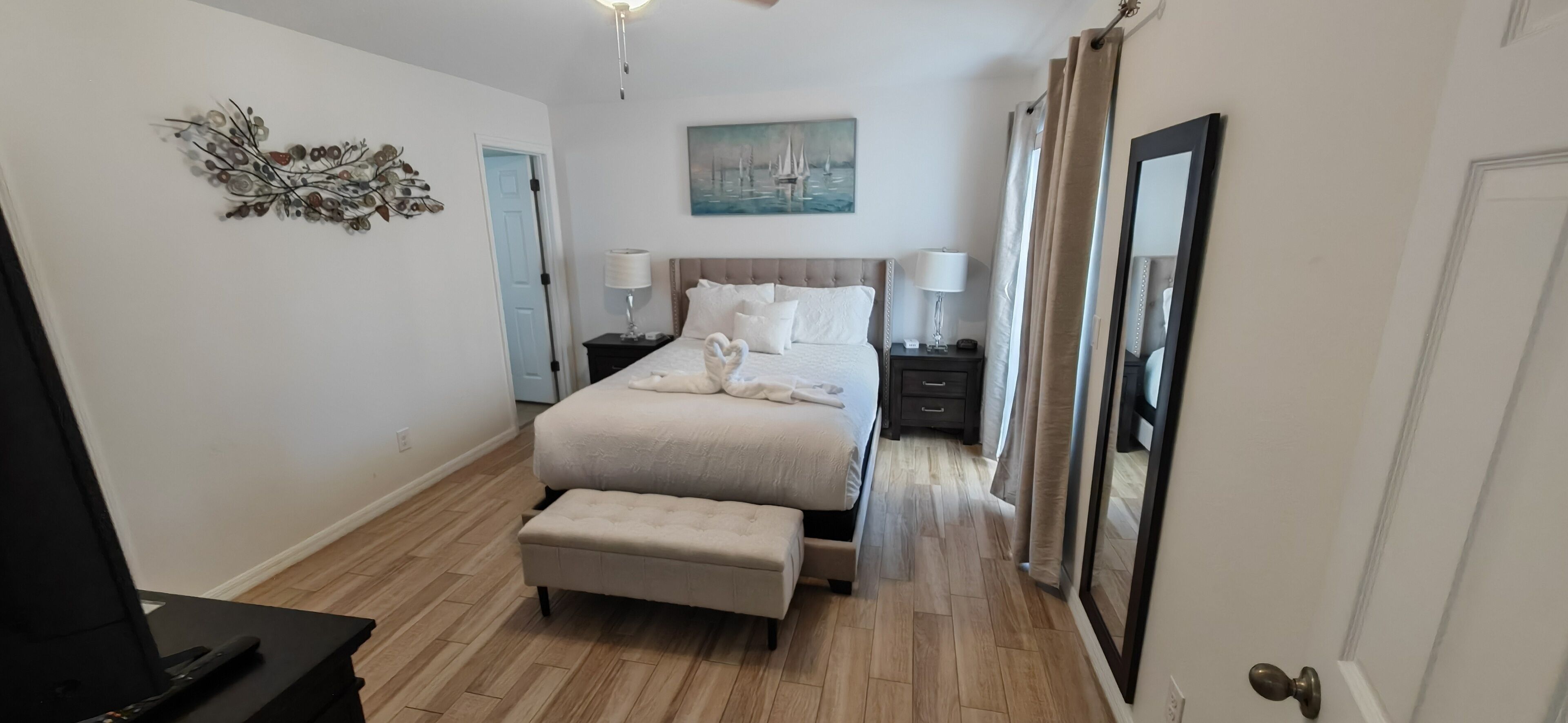 A hotel room with a bed, a bedside table, a lamp, a mirror, a door, and a wall decoration.
