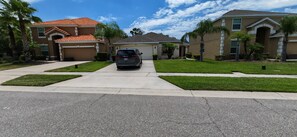 A residential street with two houses, a driveway, and a parked car. - Luxury Disney Vacation Home Private Pool Resort Amenities Sleeps 8 Game Room (Kissimmee)