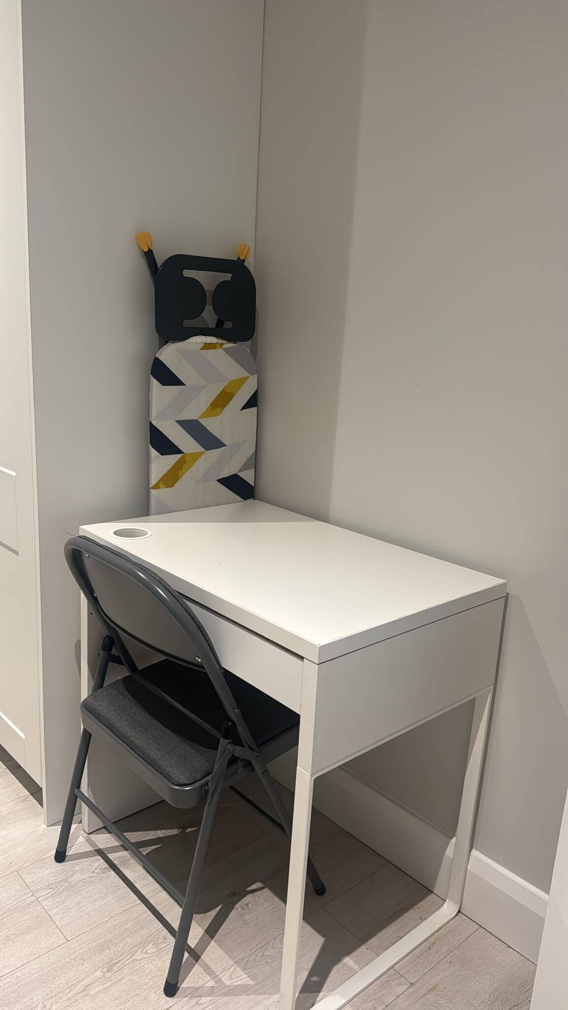 Ett hörnbord med en stol, en väggmonterad förvaringsenhet och en kudde med geometriskt mönster.