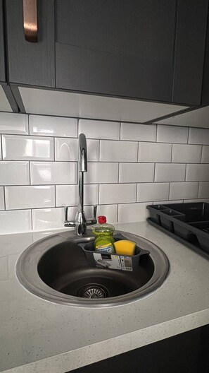 Un lavamanos de cocina con grifo, una botella de detergente y una esponja.