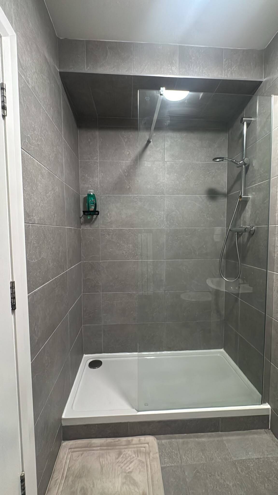 Une douche à l’italienne avec une porte en verre, un pommeau de douche à main et un autre pommeau de douche à main fixé au mur.